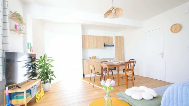 A bright, modern living room with a TV, wooden furniture, a dining table, and a kitchen in the background. - LES LOGIS DU GENERAL - Ground floor apartment (Beaupréau-en-Mauges)