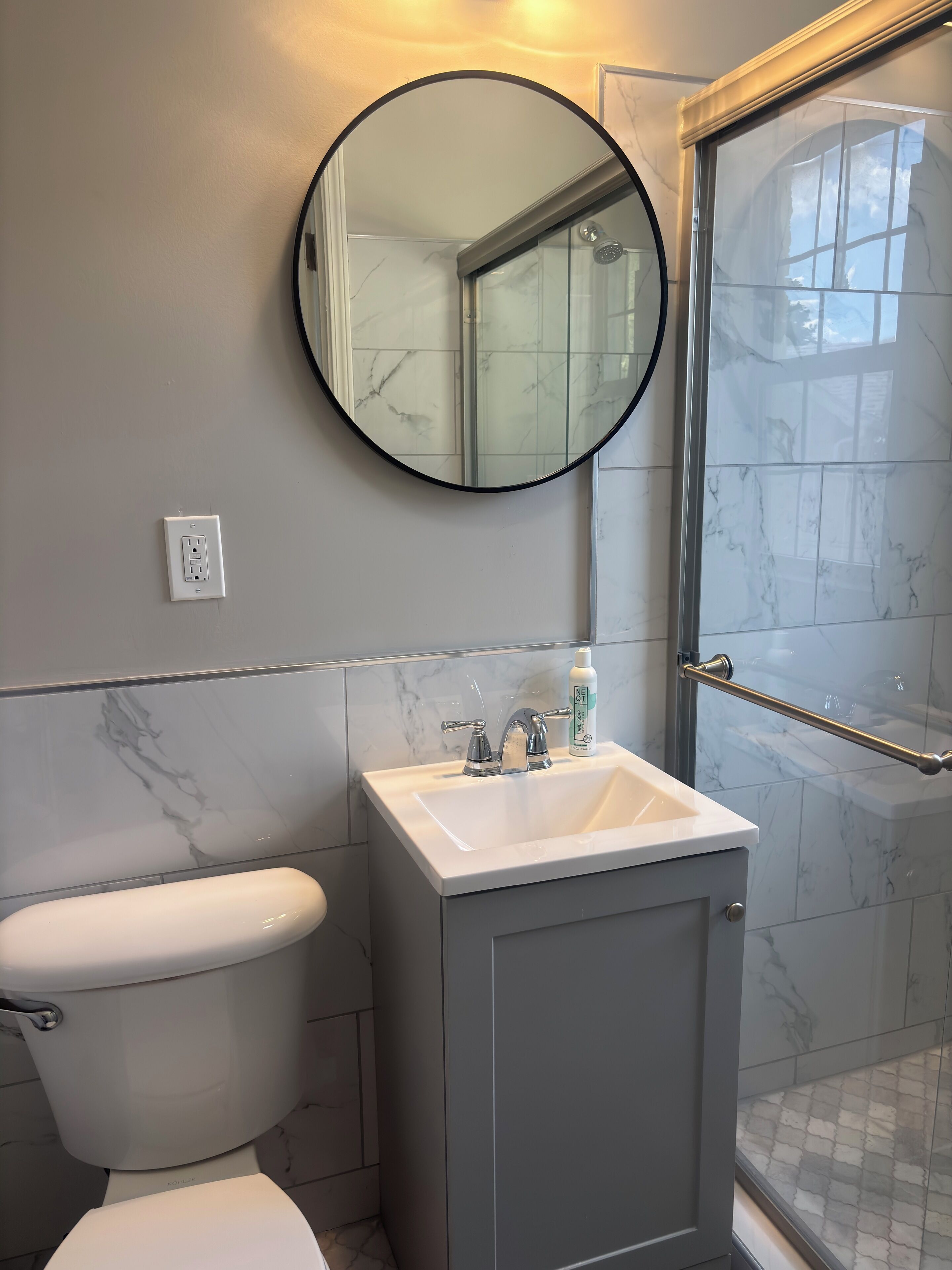 Un baño con inodoro, lavabo con espejo y zona de ducha.