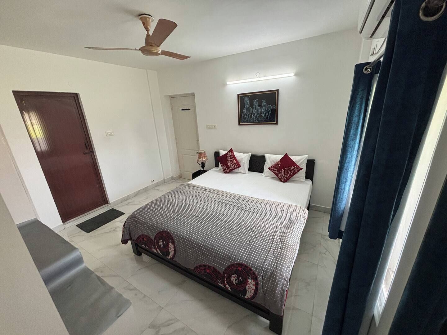 A bedroom with a bed, a ceiling fan, a door, and a wall-mounted light fixture.