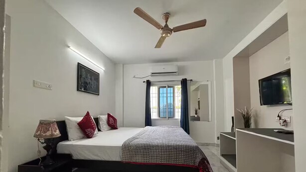 Ein Schlafzimmer mit Bett, Deckenventilator, Fernseher und einem Fenster mit Vorhängen.