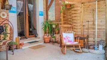 A cozy outdoor seating area with a wooden chair and table, surrounded by potted plants and a rustic wooden wall.