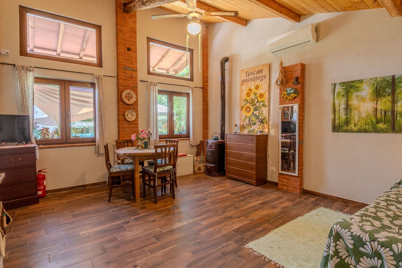 A cozy room with a wooden ceiling, a dining table with chairs, a dresser, and a painting of sunflowers.