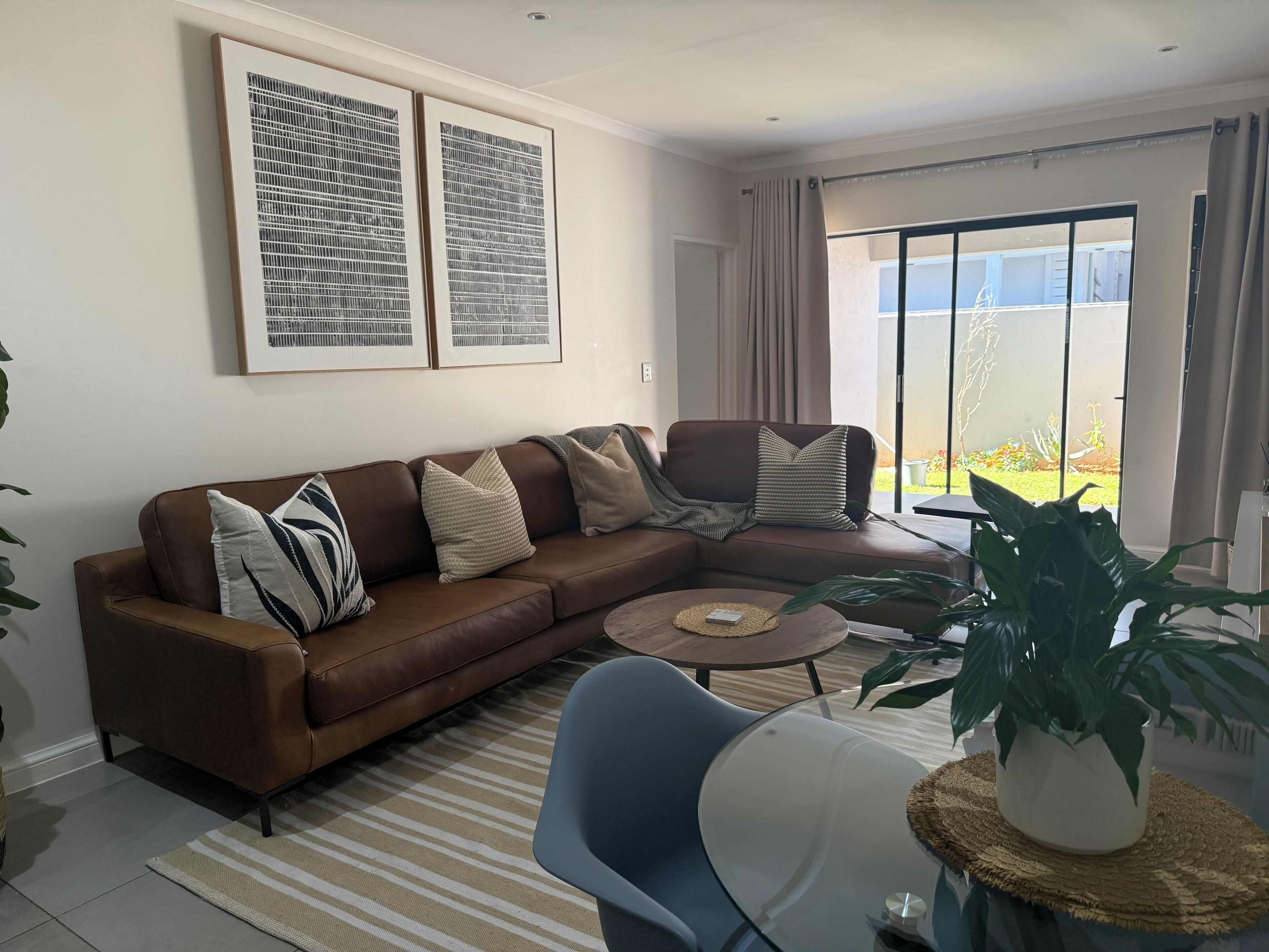 Ein Wohnzimmer mit einem braunen Ledersofa, einem Glastisch und Blick auf einen Balkon mit Pflanzen.