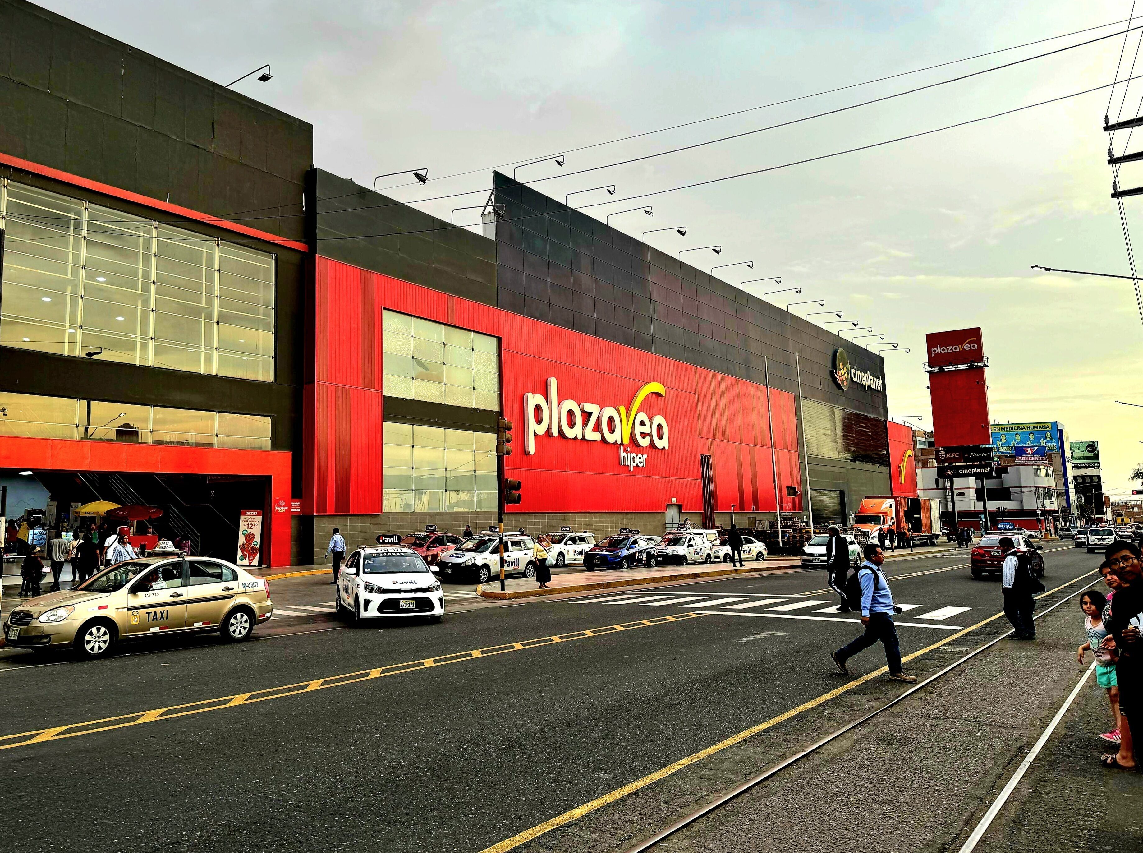 A commercial building with a large red facade, a visible entrance, and a street with vehicles and pedestrians.