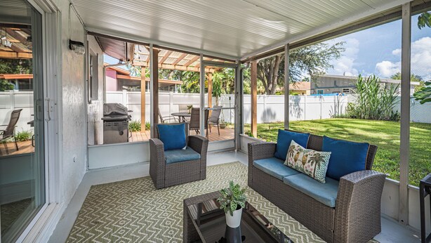 A covered patio area with wicker furniture and a grill, overlooking a backyard. - Charming 2-bedroom house in welcoming Sarasota with AC (Sarasota)