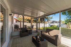 A covered patio area with wicker furniture, a grill, and a view of the backyard. - Charming 2-bedroom house in welcoming Sarasota with AC (Sarasota)