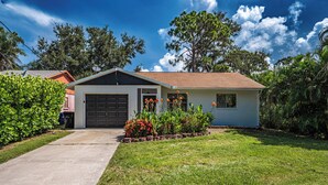 A single-story house with a garage, surrounded by a well-maintained lawn and flowering plants. - Charming 2-bedroom house in welcoming Sarasota with AC (Sarasota)