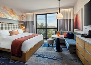 A modern hotel room with a large bed, a sofa, a small table, and a TV.