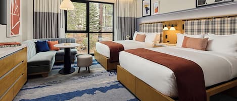 Habitación de hotel con dos camas, un sofá, una mesita y vistas a árboles a través de amplias ventanas.
