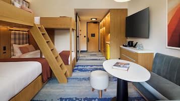 Quarto de hotel pequeno com cama beliche, um sofá compacto, mesa e televisão.
