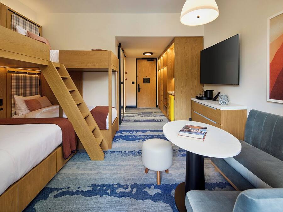 Quarto de hotel pequeno com cama beliche, um sofá compacto, mesa e televisão.