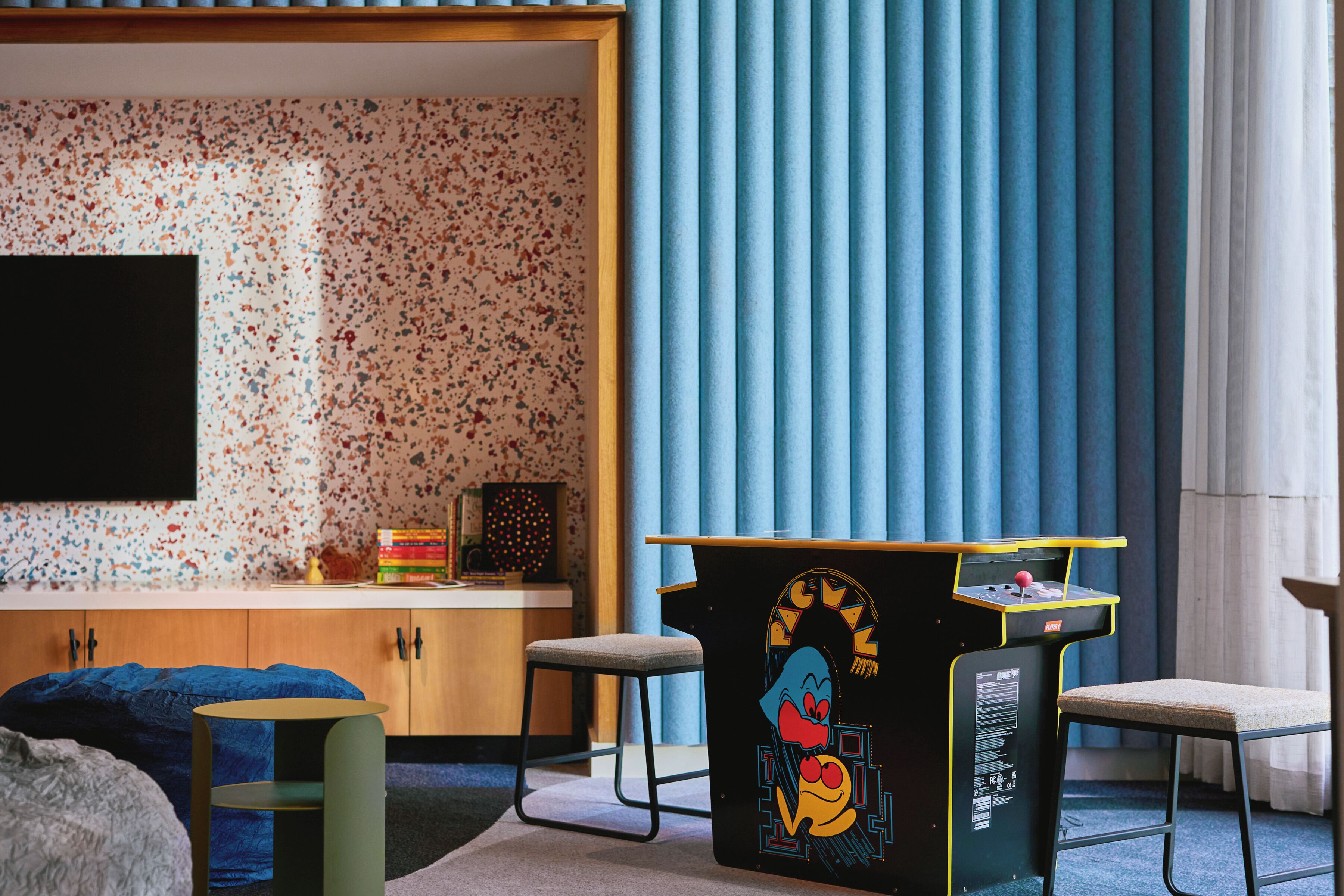A modern room with a speckled wallpaper, a flat-screen TV, a desk with a cartoon character, and a blue curtain.