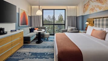Una habitación de hotel moderna con una cama grande, un sofá, un escritorio y un televisor. Hay una ventana con vistas a árboles.