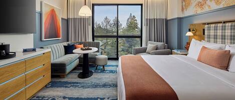 Une chambre d’hôtel moderne avec un grand lit, un canapé, un bureau et une télévision. Il y a une fenêtre donnant sur des arbres.
