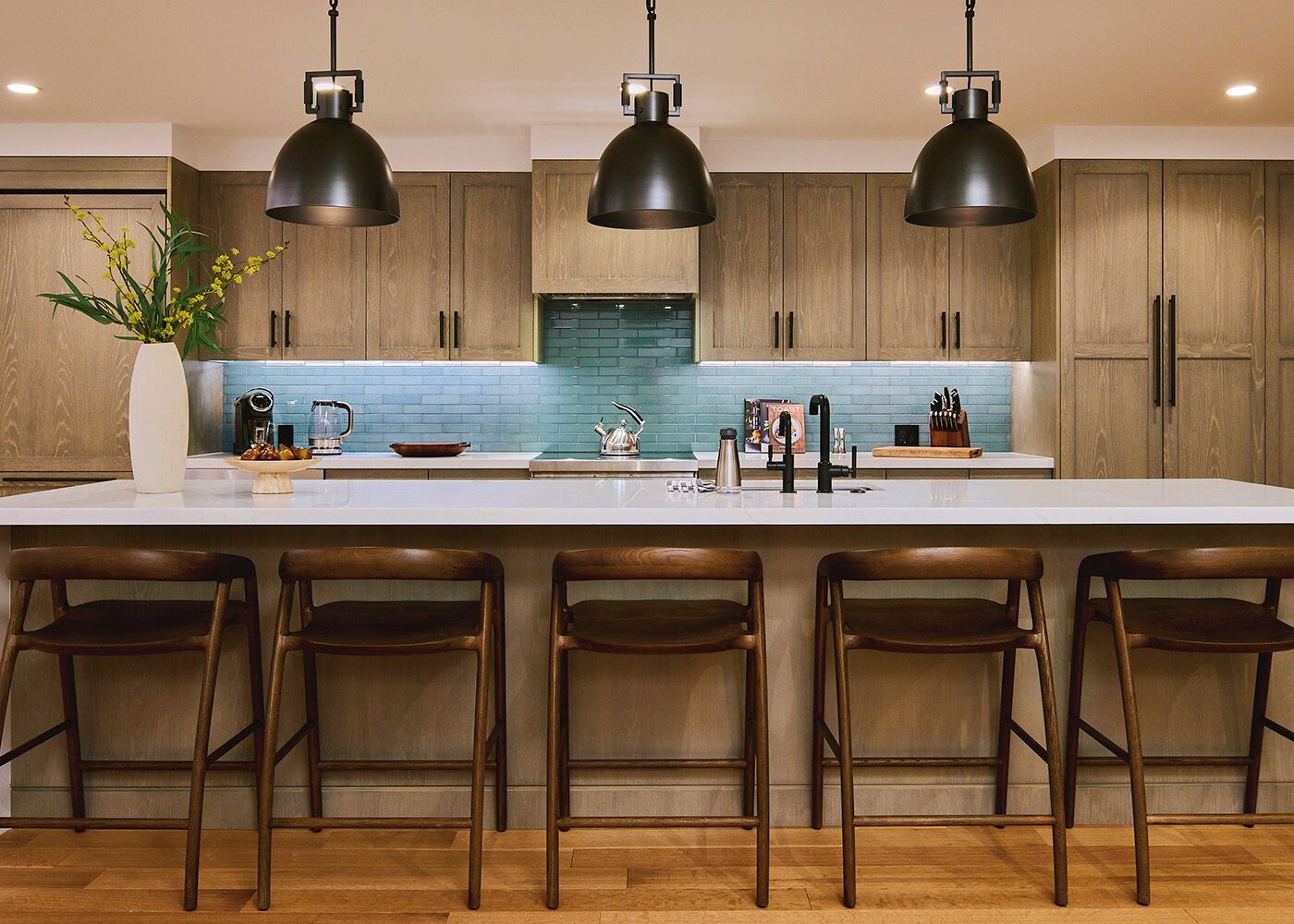 A modern kitchen with a large island, wooden cabinets, and pendant lighting.