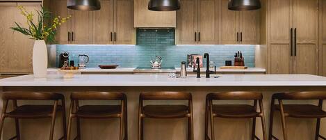 Una cocina moderna con una isla grande, armarios de madera e iluminación colgante.