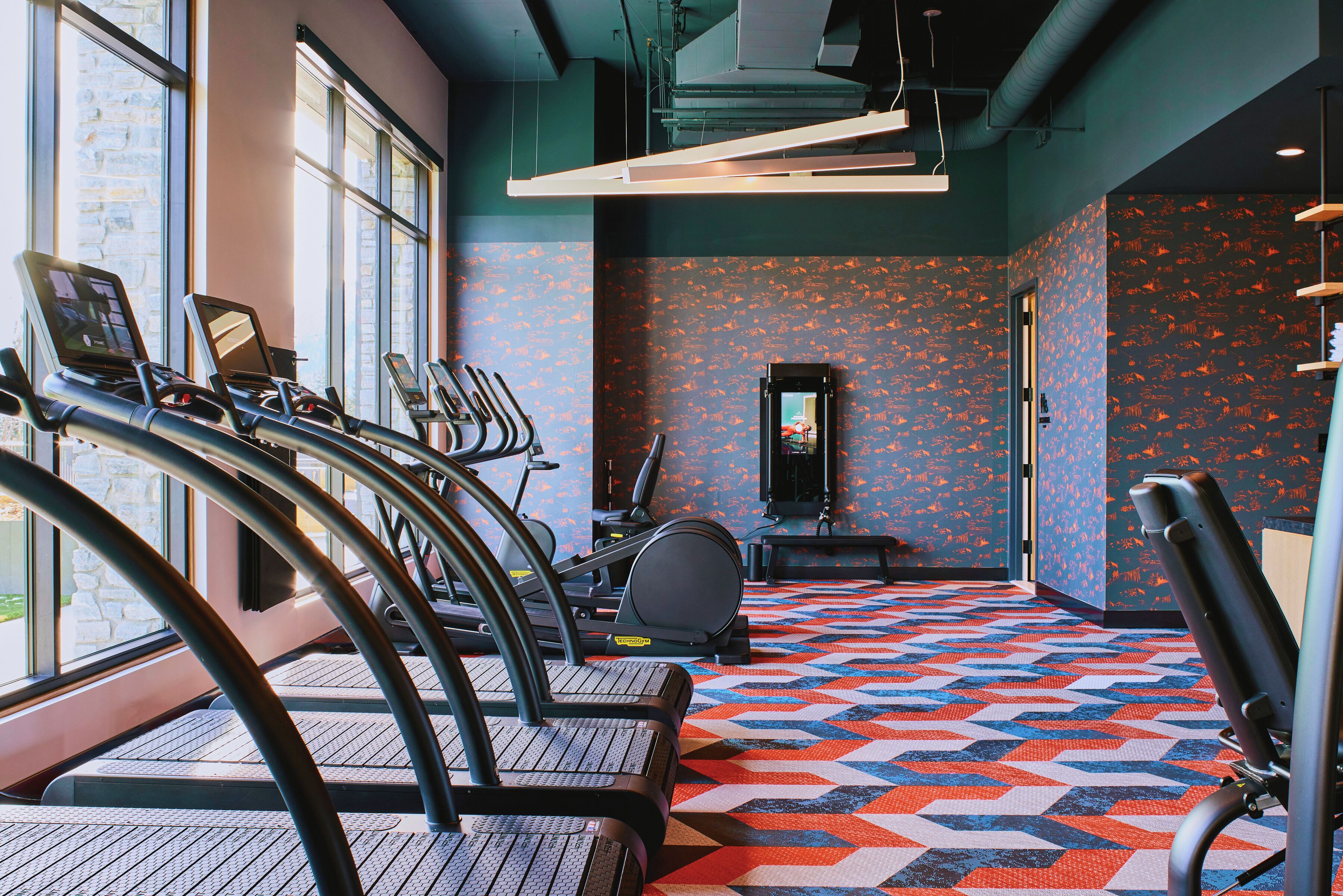 Een fitnessruimte met loopbanden, een hometrainer en een spiegel.