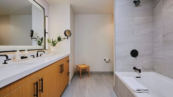 Un baño moderno con un espejo grande, un lavamanos con lavabo, una ducha con cabezal de lluvia y un taburete pequeño de madera.