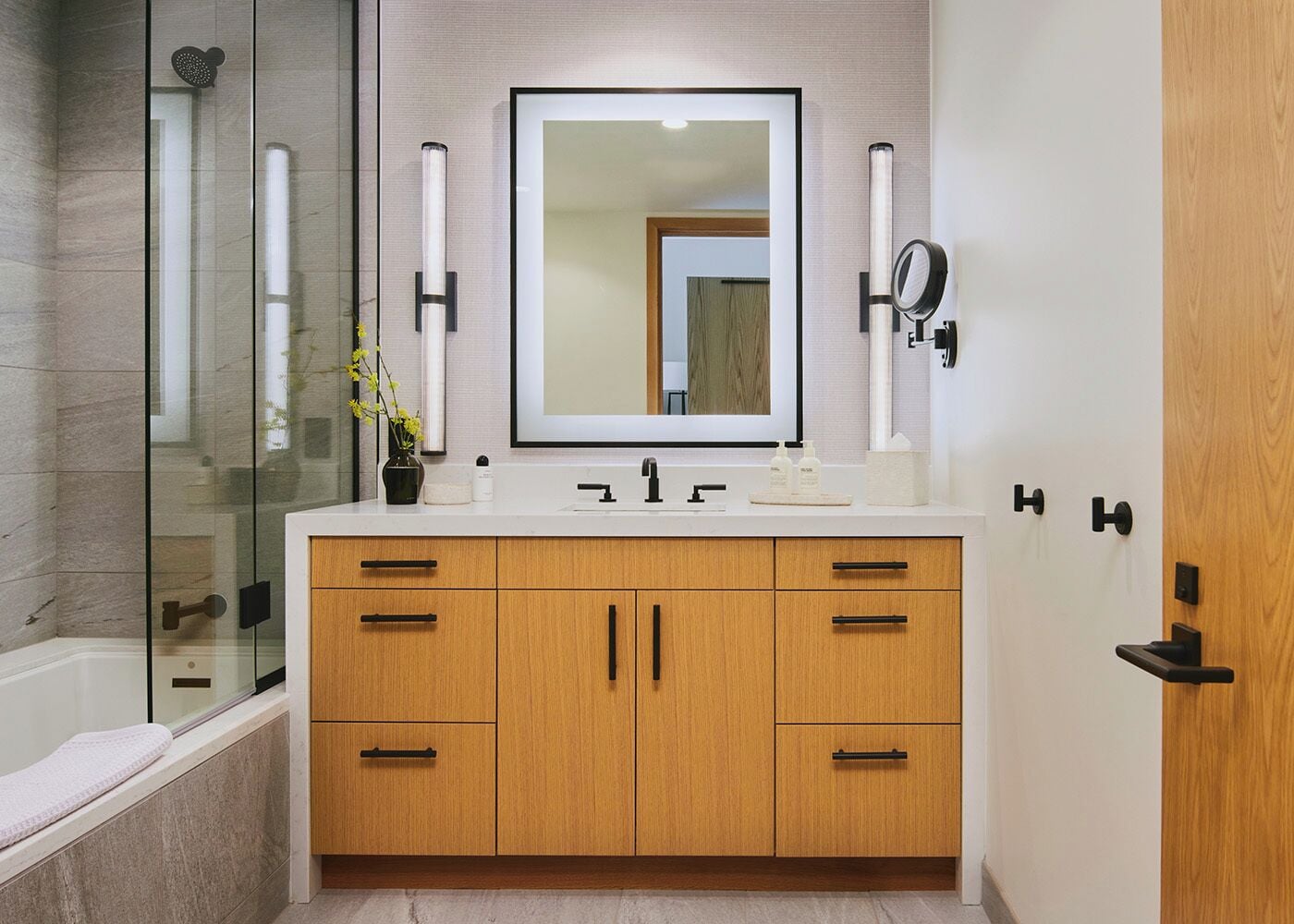 Un baño moderno con cabina de ducha de vidrio, un espejo grande, armarios de madera y encimera blanca.