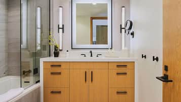 A modern bathroom with a glass shower enclosure, a large mirror, wooden cabinets, and a white countertop.