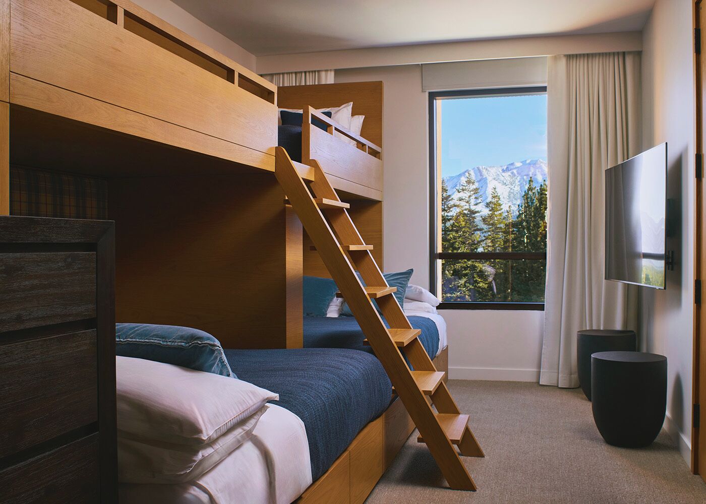 A room with bunk beds, a TV, a window with a mountain view, and a staircase.