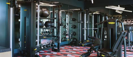 Un gimnasio con diversos equipos de ejercicio, incluyendo máquinas de pesas, pesas libres y máquinas de cardio.
