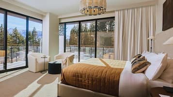 A modern hotel room with a large bed, a sitting area, and a balcony with a mountain view.