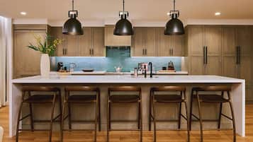 A modern kitchen with a large island, bar stools, pendant lights, and wooden cabinets.