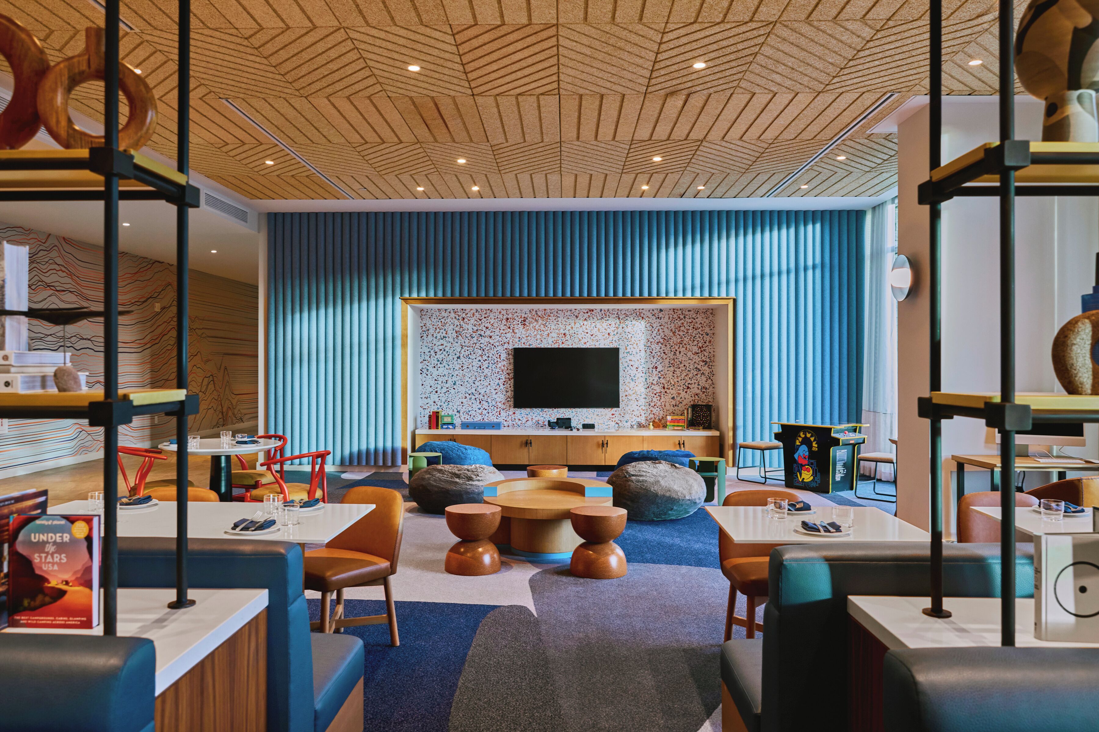 A modern interior with a central seating area, a flat-screen TV mounted on a textured wall, and a ceiling with a geometric pattern.