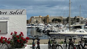 A marina with boats docked, a sign reading 'Port Soleil', and bicycles parked in the foreground.