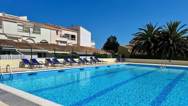 A swimming pool with blue tiles, surrounded by lounge chairs and a building with a tiled roof.