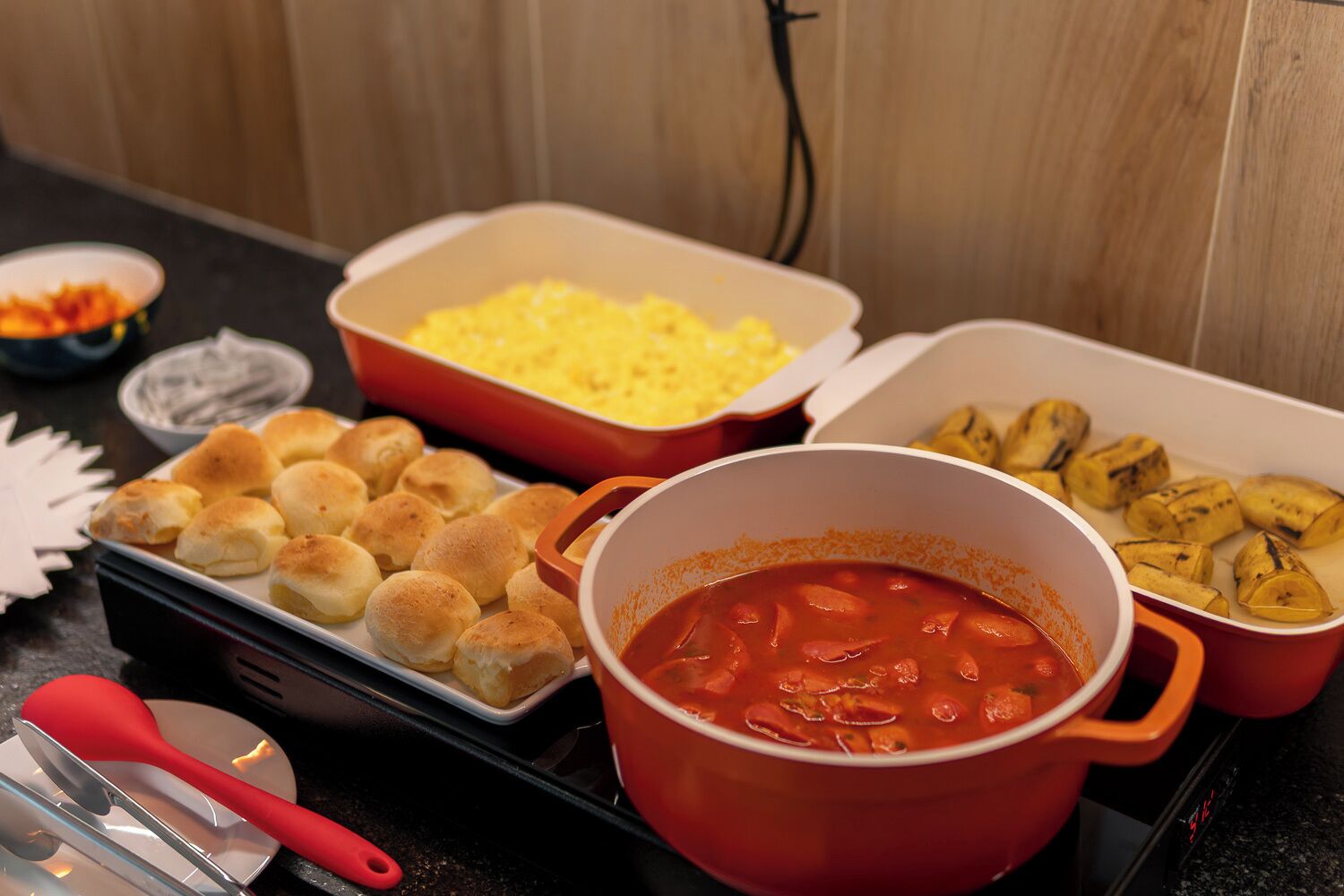 Une table de buffet proposant divers plats, notamment des petits pains, une soupe rouge et un plat en gratin.