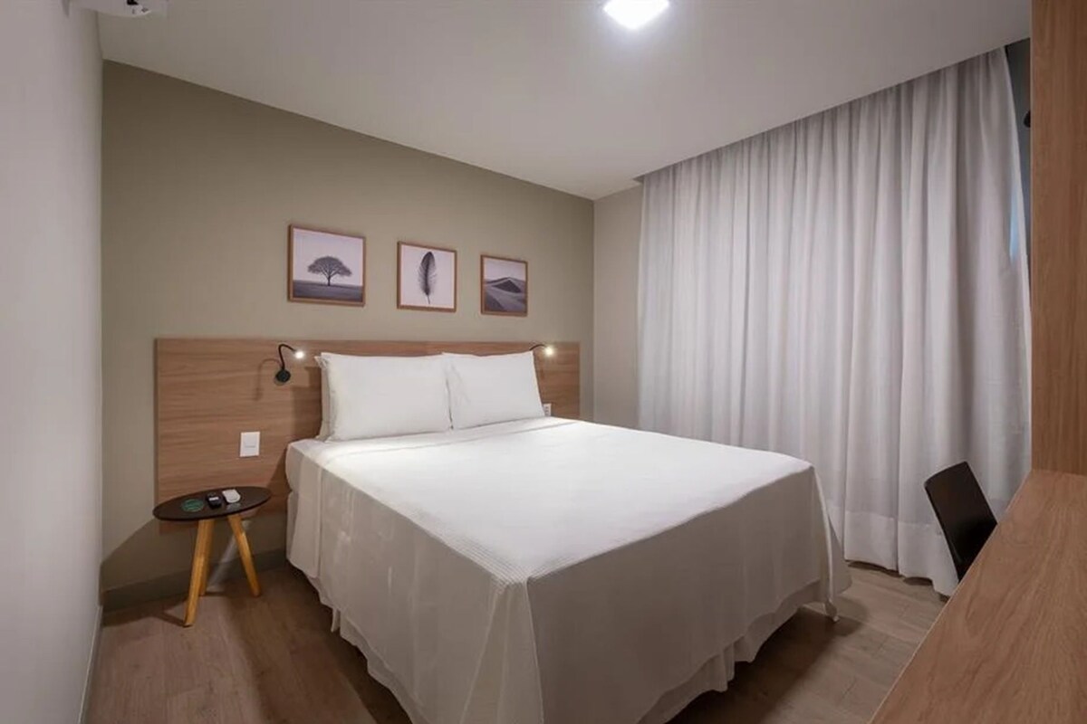 Ein Hotelzimmer mit einem Bett, einem kleinen Tisch, einem Sessel und drei gerahmten Bildern an der Wand.