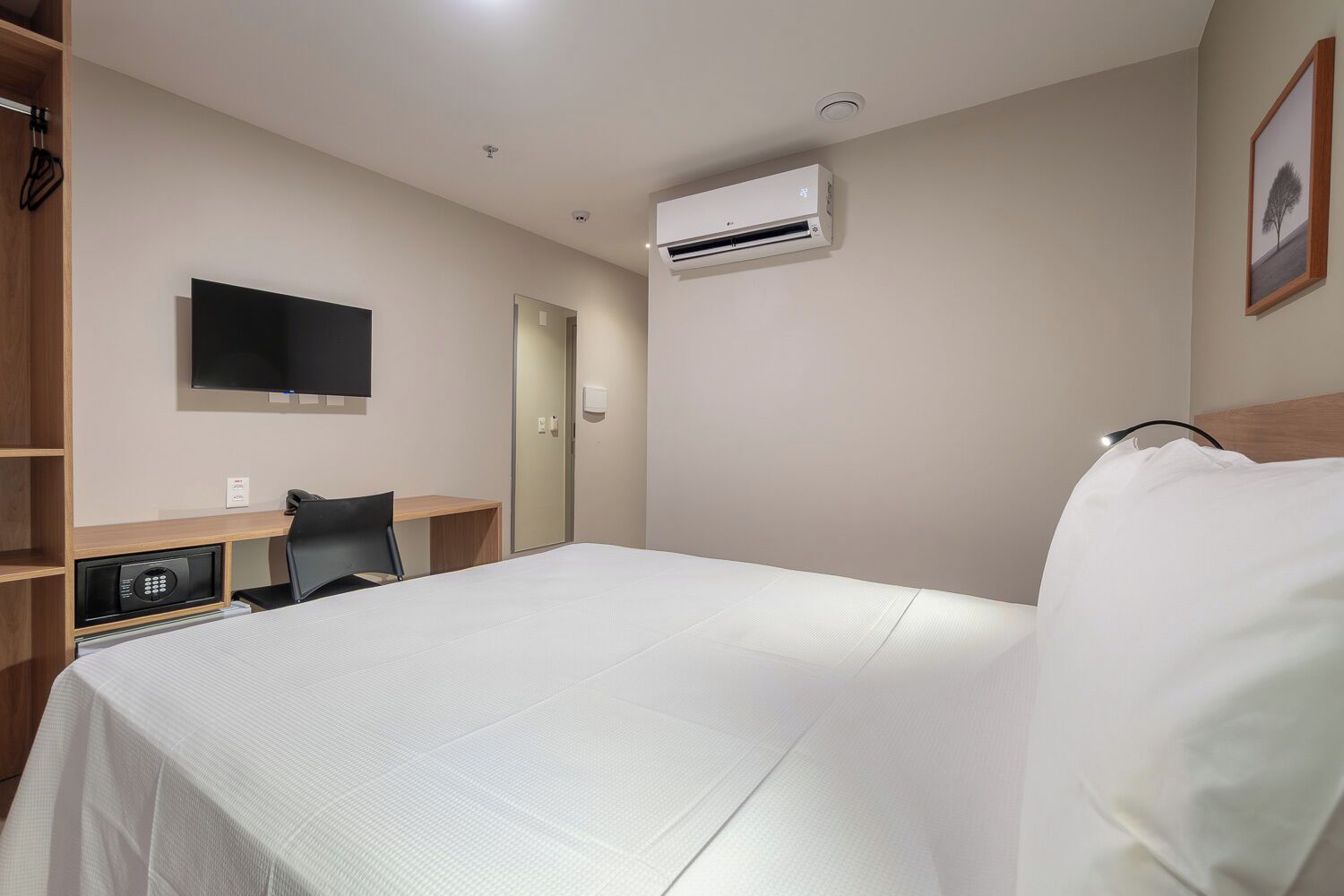 Una habitación de hotel con cama, escritorio, silla, televisor y aire acondicionado.