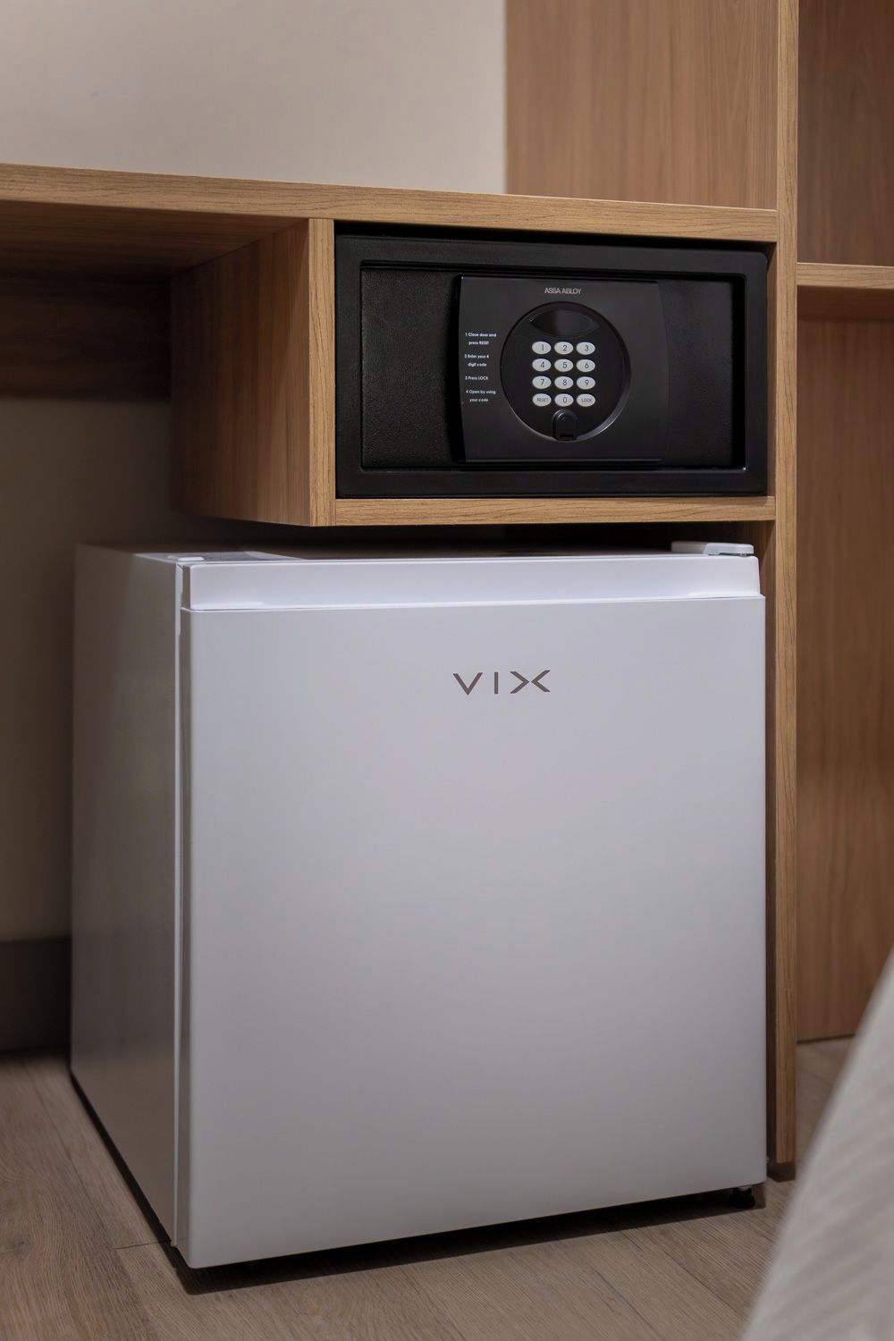 Un refrigerador compacto con un microondas incorporado encima, ubicado en un mueble de madera.