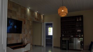 Amplia sala de estar con pared de piedra, un televisor de pantalla plana grande, un mueble de entretenimiento de madera, una lámpara colgante y una estantería.