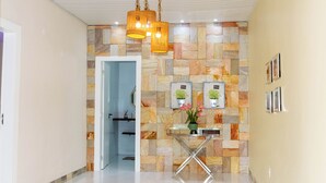 Un pasillo con pared de piedra, una consola de vidrio con un florero y una lámpara colgante.