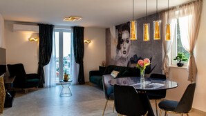 A modern living room with a round dining table, black chairs with gold legs, a green sofa, and a large abstract painting on the wall. - Apartments Sweet Escape - Two Bedroom Apartment with Terrace and Sea View (Dubrovnik)