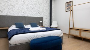 A modern bedroom with a large bed, a grey headboard, a bedside table with a lamp, a wooden bench, and a framed picture on the wall. - Les Genêts - PMR gîte - pets welcome (Saint-Christophe-du-Bois)