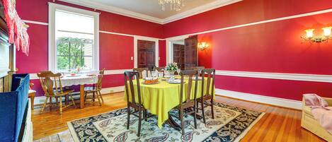 Uma sala de jantar com parede vermelha, um candelabro, uma mesa de madeira com cadeiras e um tapete estampado.