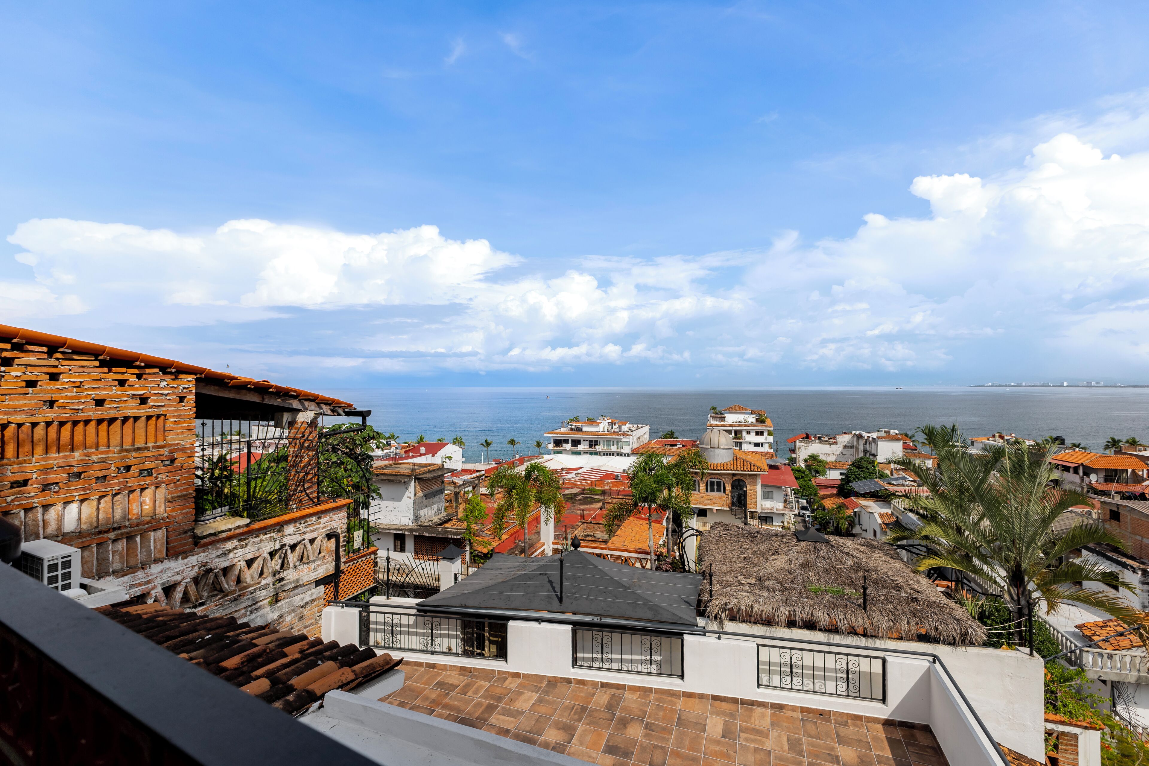A coastal town with terracotta-roofed buildings, a thatched-roof structure, and a view of the sea.