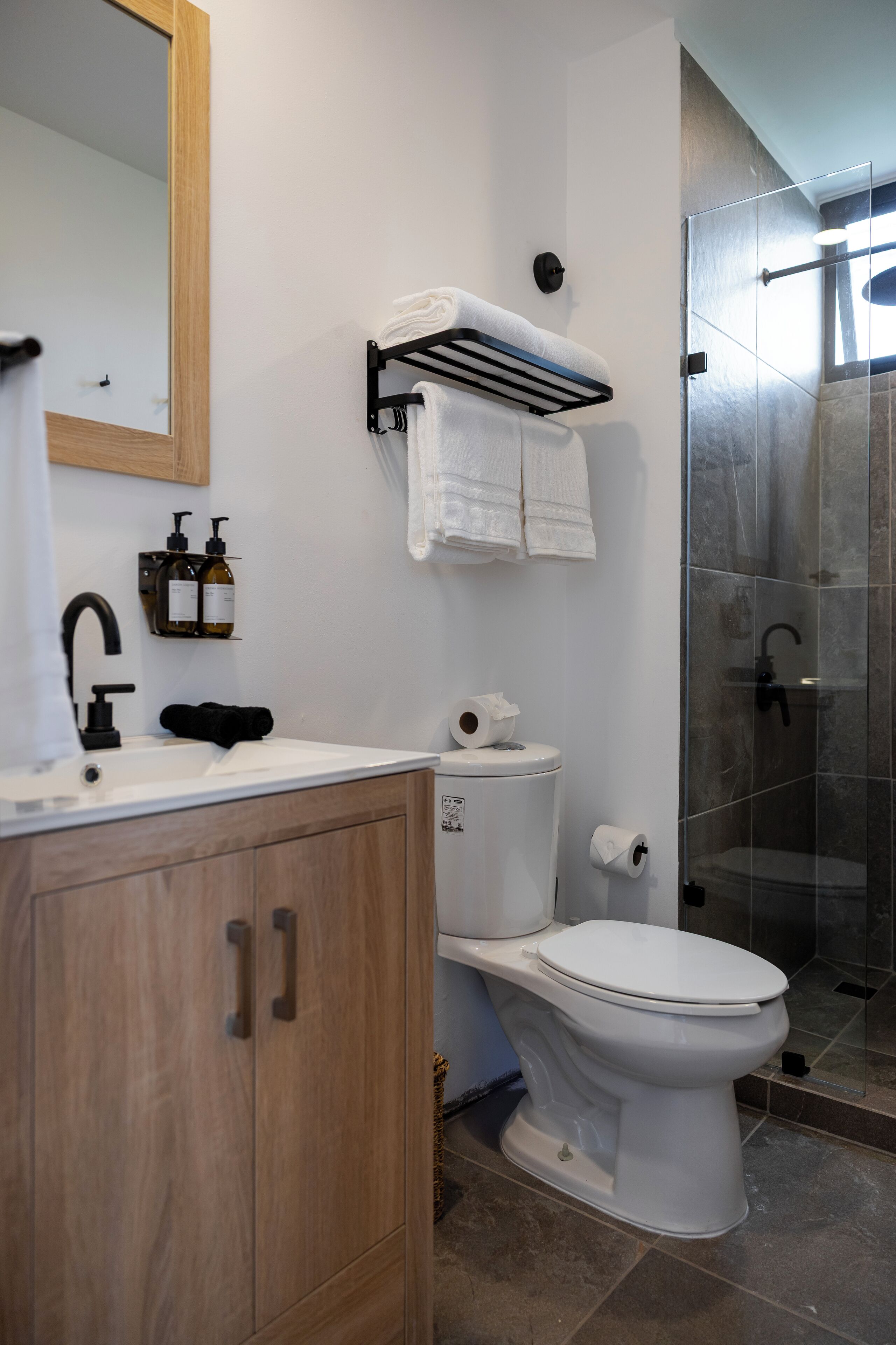 Ein modernes Badezimmer mit einem Holzkabinent, einer weißen Toilette, einem schwarzen Wasserhahn und einer Duschkabine aus Glas.