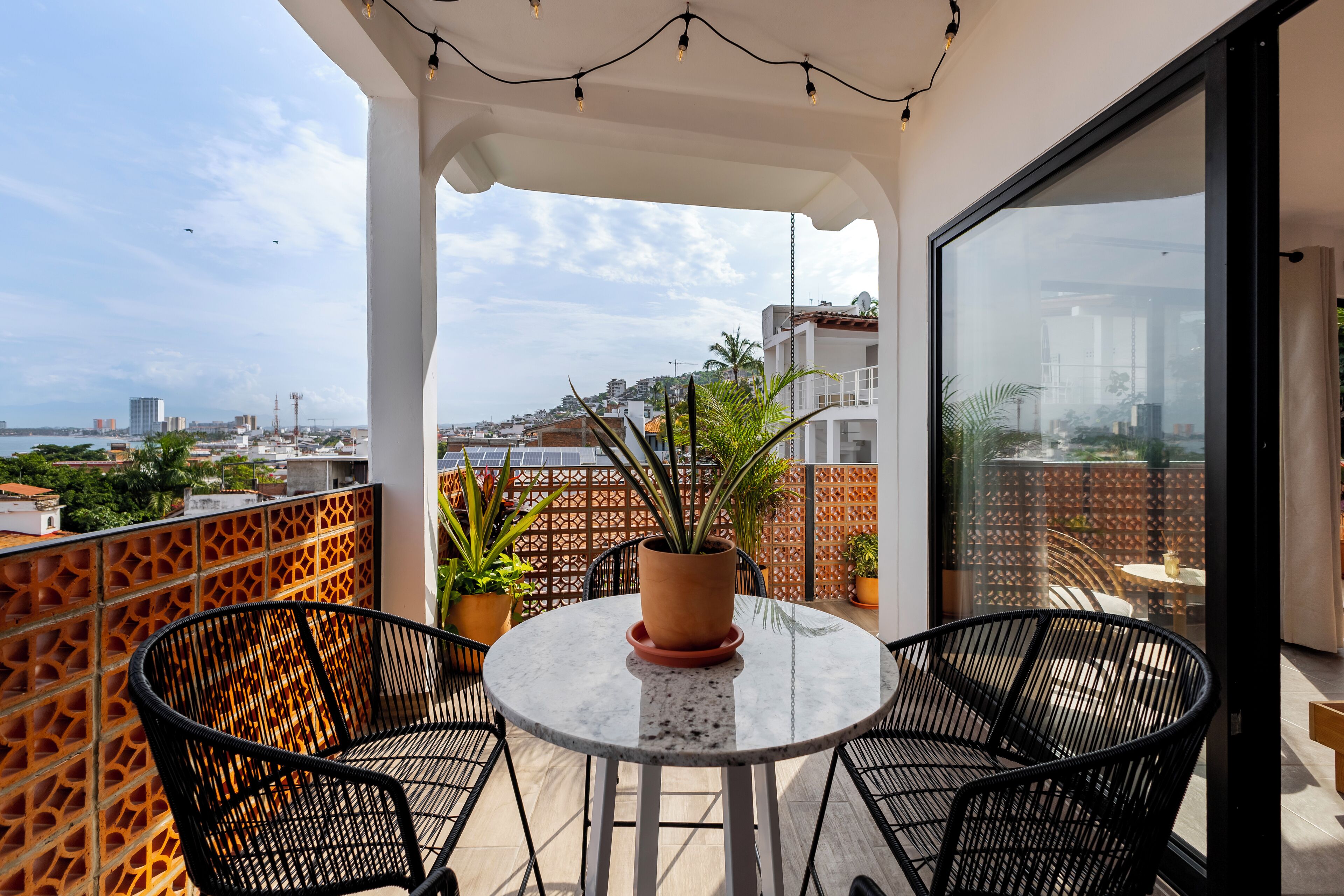 Un balcon avec une table ronde et des chaises, des plantes en pot et une vue sur le paysage urbain.