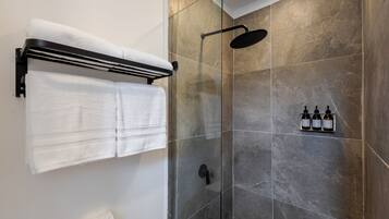 A modern bathroom with a glass shower enclosure, a towel rack with two white towels, and a set of toiletries on the wall.