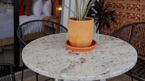 Una mesa redonda con una planta en maceta, sillas negras y vistas de un dormitorio con cama y mesita de noche.