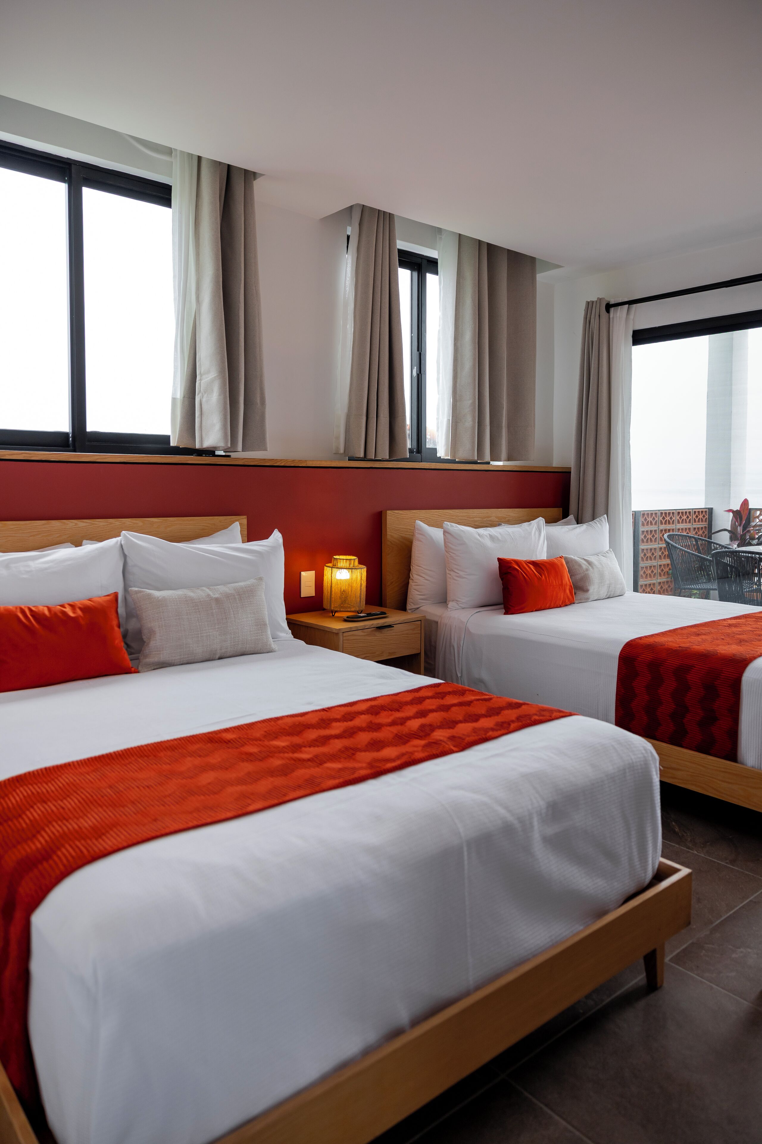 Ein Hotelzimmer mit zwei Betten, beigen Vorhängen, einem Nachttisch mit Lampe und Blick ins Freie.