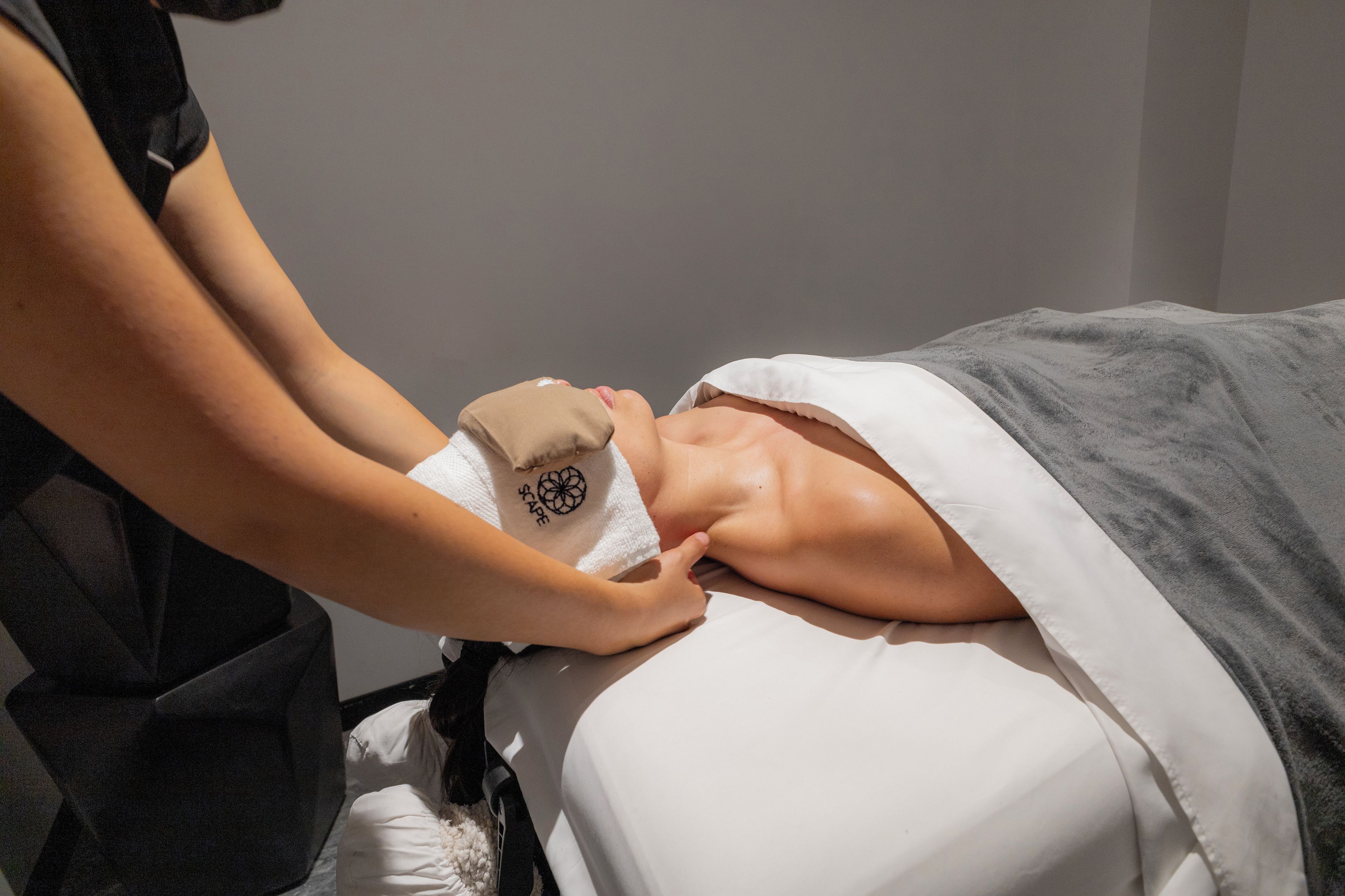 A person lying on a bed with a white blanket, receiving a massage.