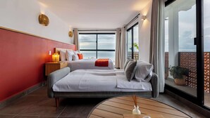 Un hotel moderno con una cama grande, una mesita de noche con lámpara y vistas al mar a través de amplias ventanas.
