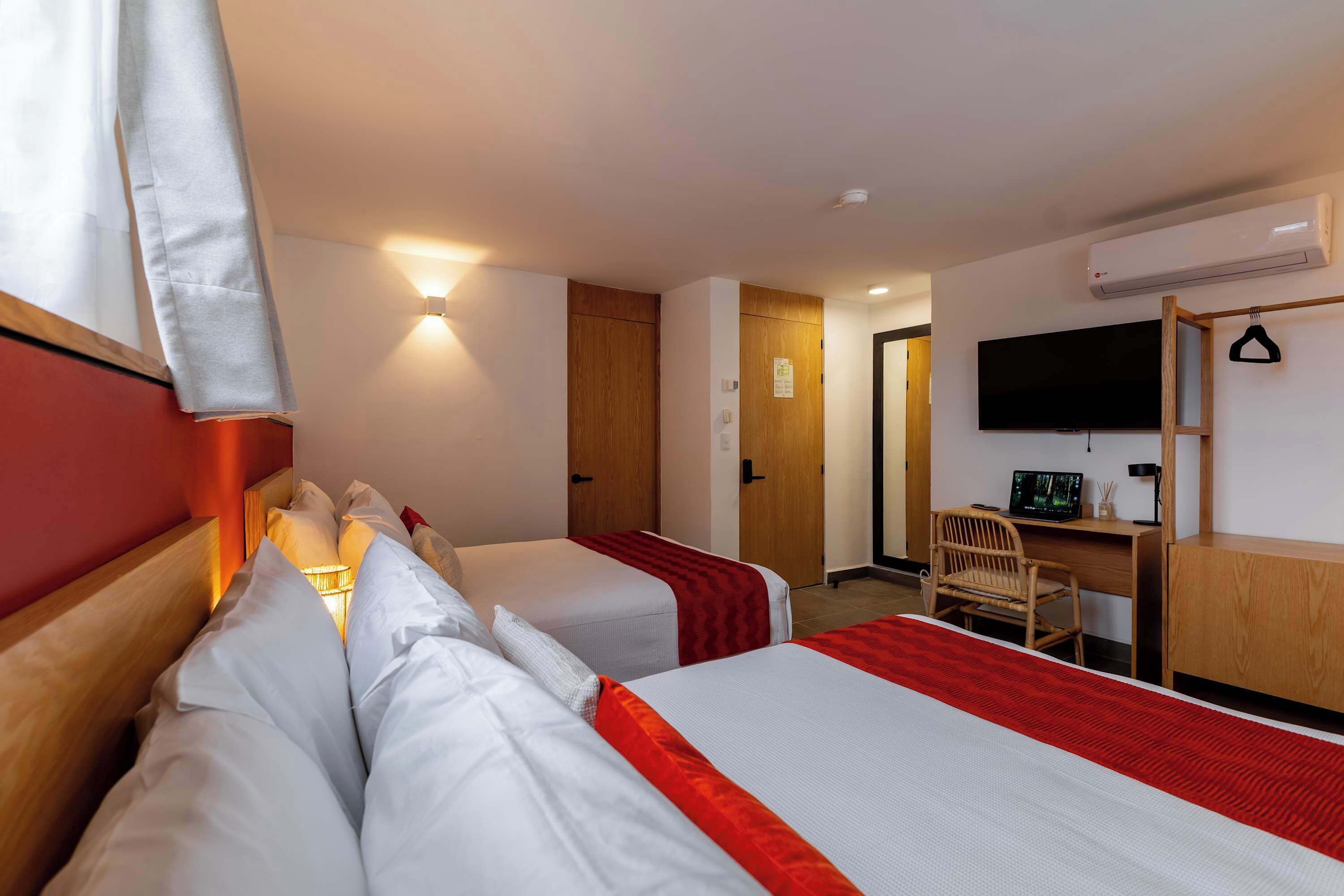 A hotel room with two beds, a desk, a chair, a television, and an air conditioning unit.