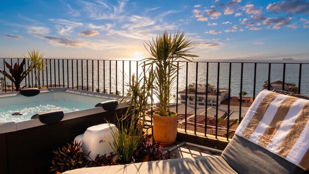 Una piscina en la azotea con vista al mar, rodeada de plantas en macetas y una toalla a rayas.